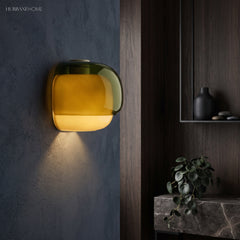Green dual-tone glass wall sconce lit against a dark blue plaster wall