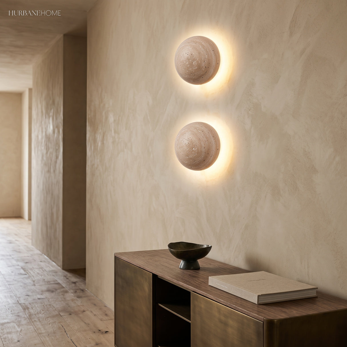 Two stone wall sconces glowing on a plaster hallway wall above a console