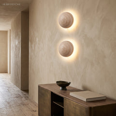 Two stone wall sconces glowing on a plaster hallway wall above a console