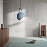 Blue pendant light angled against a concrete wall above a walnut sideboard