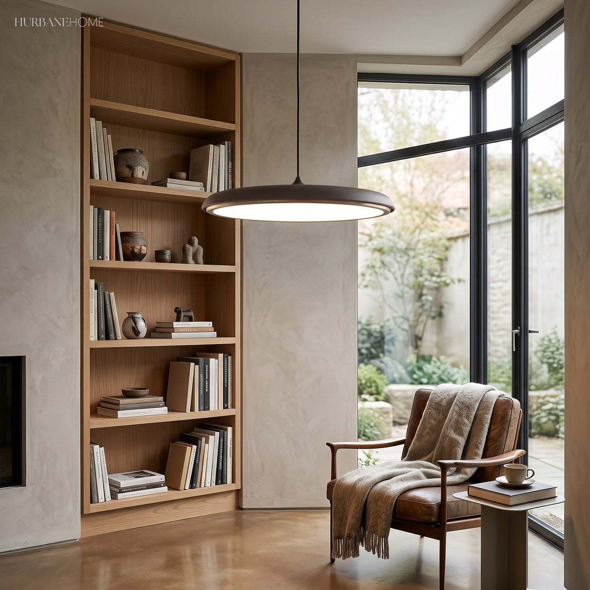 Black disc pendant light suspended over a bookshelf and leather reading chair