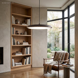 Black disc pendant light suspended over a bookshelf and leather reading chair