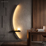 Black minimalist crescent LED sconce lighting a warm walnut home office wall