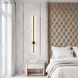 Vertical black wall sconce on a marble wall beside a tufted bedroom headboard