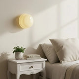 Light yellow glass wall sconce above a white bedside table daylight