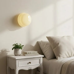 Light yellow glass wall sconce above a white bedside table daylight