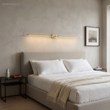 Gold linear LED sconce mounted horizontally above an upholstered bed