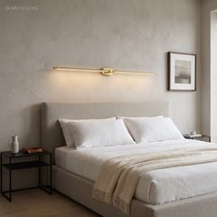Gold linear LED sconce mounted horizontally above an upholstered bed