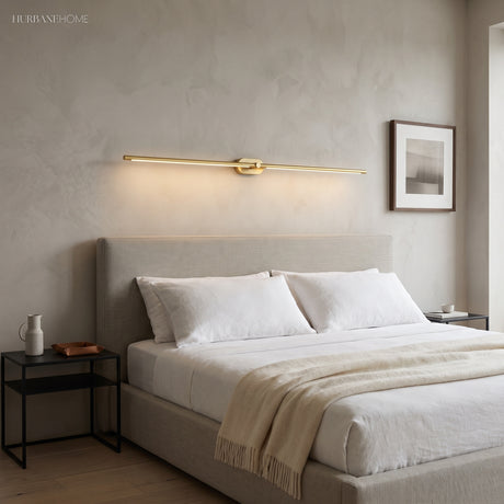 Gold linear LED sconce mounted horizontally above an upholstered bed