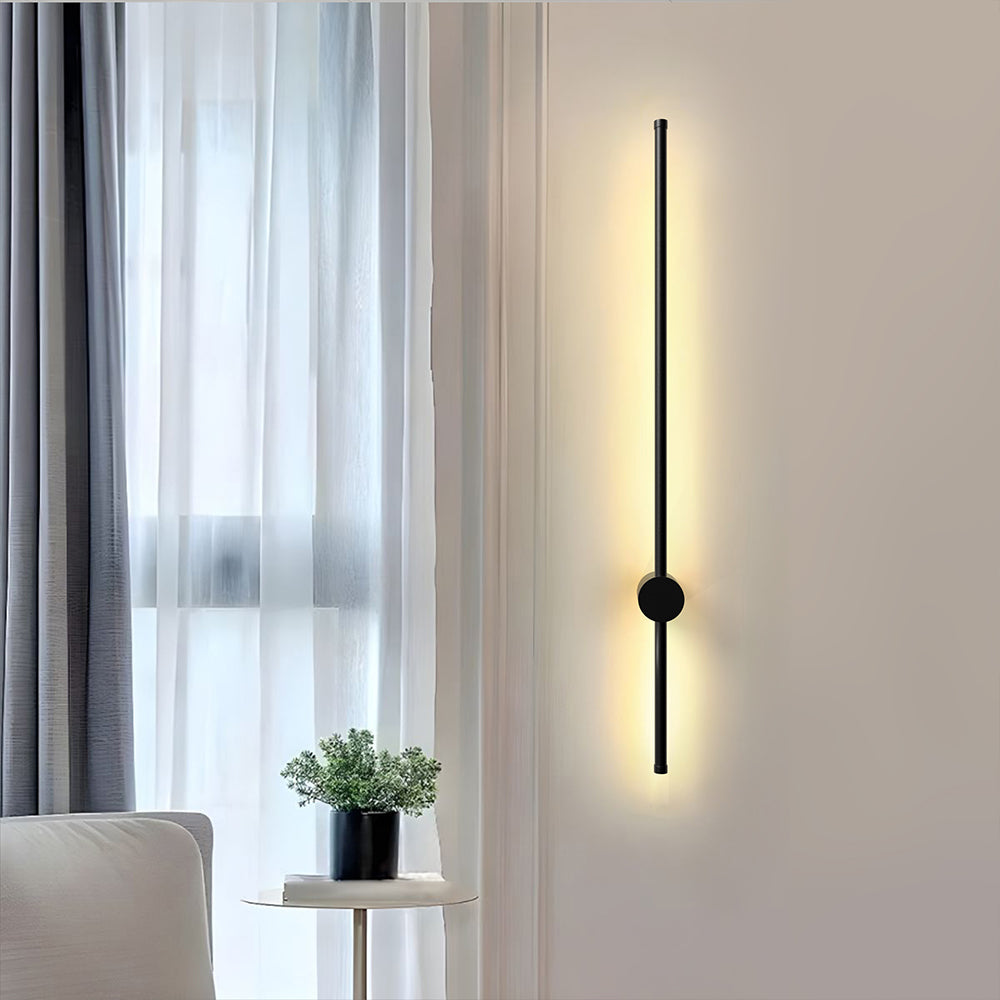 Single vertical black linear wall light on a beige wall next to a plant