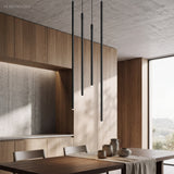 Staggered black tube pendant lights above a dining table in a wood kitchen