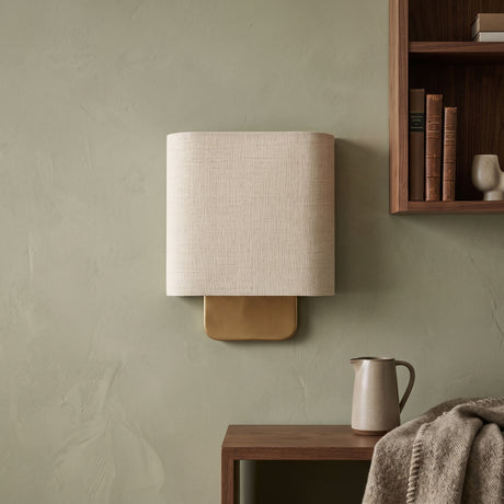 Natural linen shade wall sconce with brass backplate on a green wall