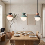 Three macaron pendant lights in pink, grey and blue hanging above a dining table