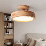 Natural wood round flush mount LED ceiling light above a bed near a rattan bookshelf
