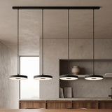 Four black disc LED pendants on a linear ceiling bar over an island