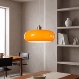 Orange oval glass pendant light hanging beside a plaster wall and shelving