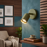 Green adjustable LED wall sconce with rotatable cylindrical shade on blue plaster wall