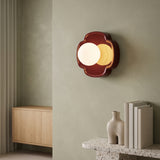 Red flower-shaped resin wall sconce with white glass globe on a sage wall