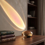 Oval glass ambient table lamp lit warm on a wooden desk by books