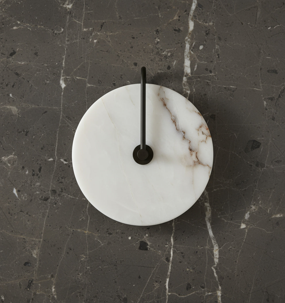Unlit marble disc on a black arm against dark veined stone