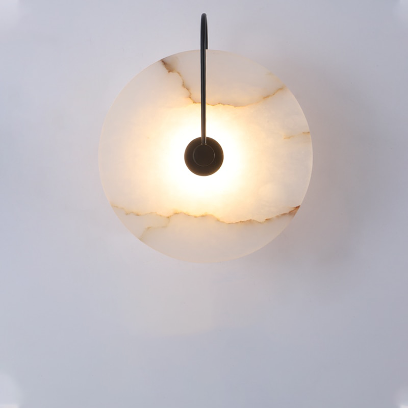 Marble disc sconce on a black curved arm against a pale wall