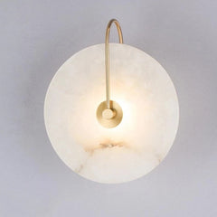 Marble disc sconce on a gold curved arm against a pale wall