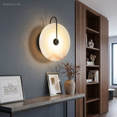 Marble disc sconce glowing above a console table and framed prints