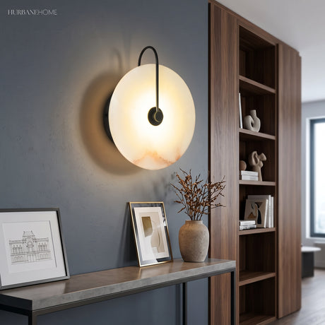 Marble disc sconce glowing above a console table and framed prints