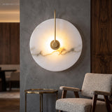 Marble disc wall light lit beside a wooden panel and armchair