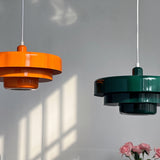 Orange and green tiered metal pendants in sunlight beside pink roses