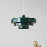 Dark green tiered metal pendant light photographed against a pale grey wall