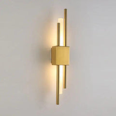 Brushed gold twin bar sconce lit against a plain grey background