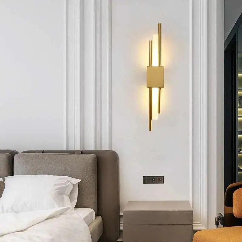 Gold linear sconce lit above a bed with a pale upholstered headboard