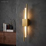 Gold twin bar sconce lit on a dark grey wall beside a cabinet