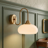Curved milk glass wall sconce with copper arm on green panelled wall