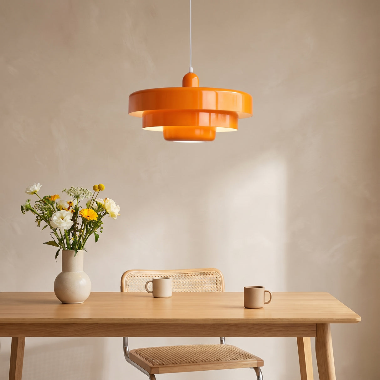 Orange tiered pendant light above an oak dining table with a vase of flowers