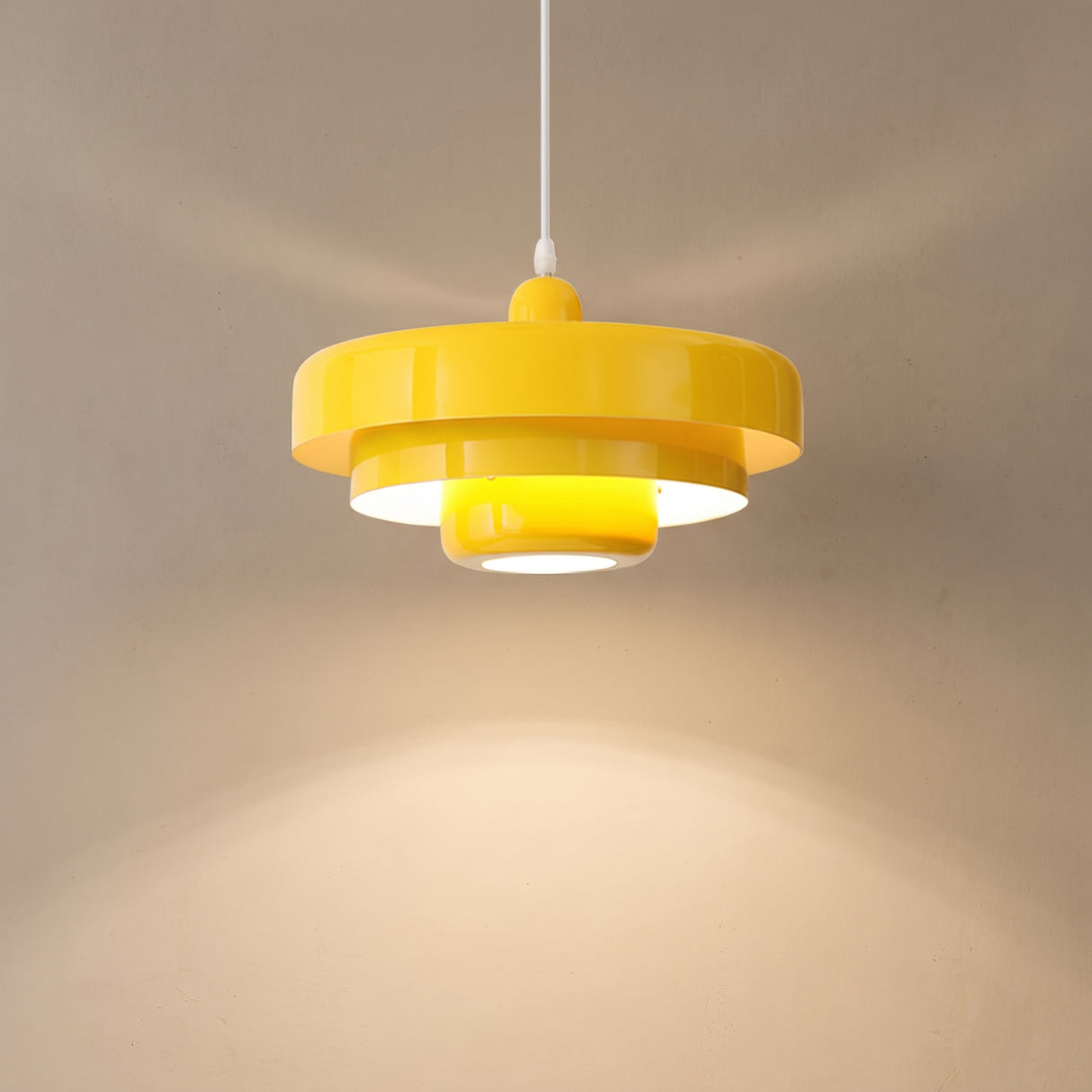 Yellow tiered pendant light casting a warm cone of light down a beige wall