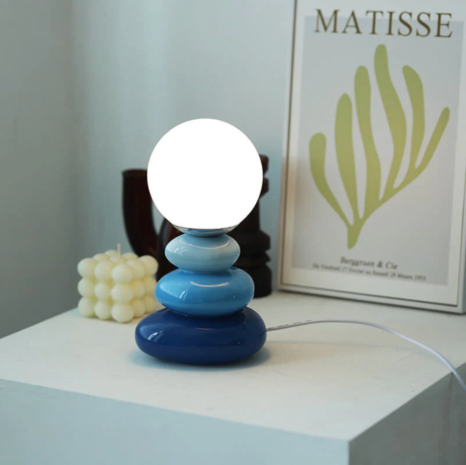 Blue stacked lamp glowing in front of a framed botanical poster