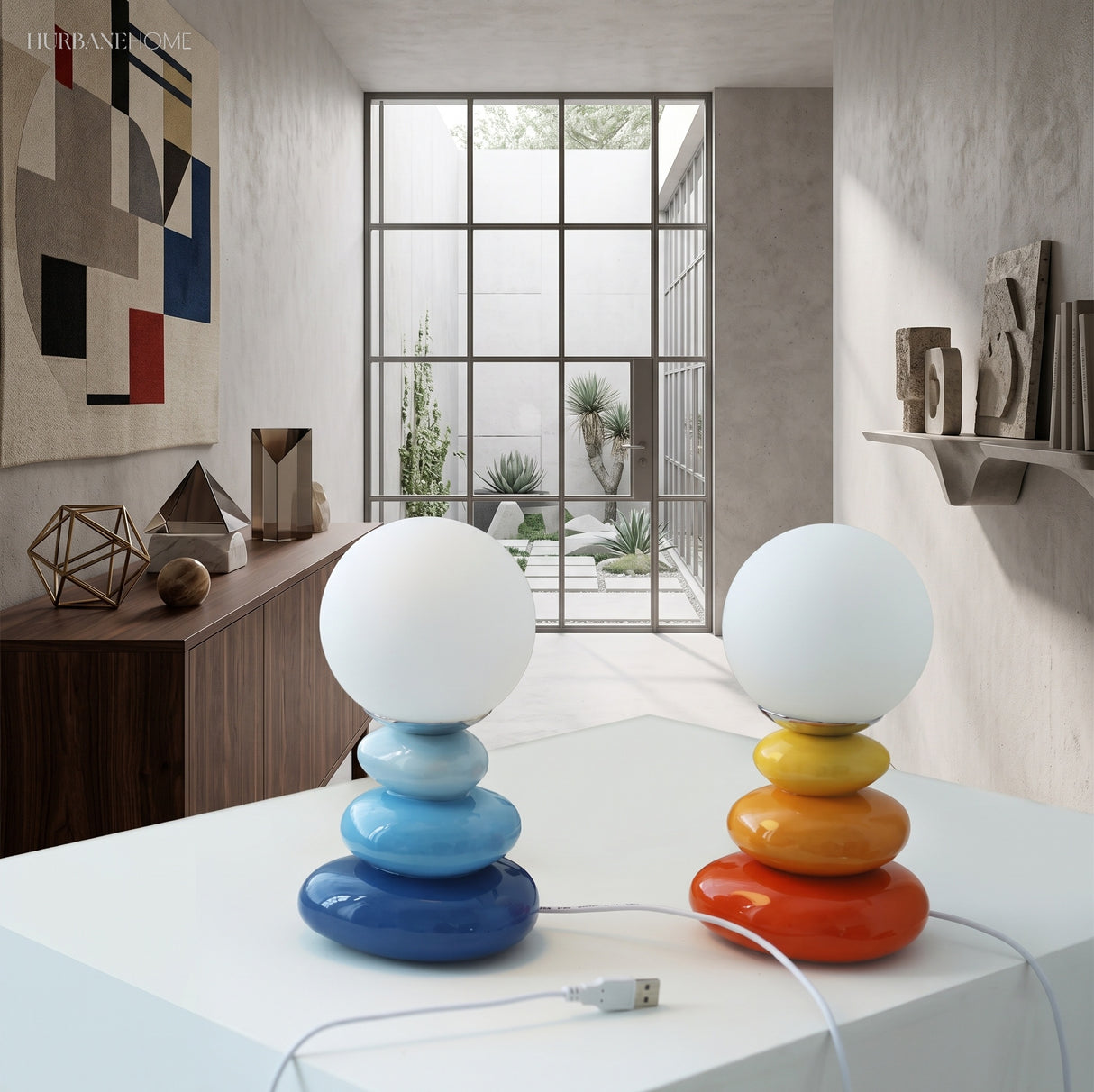Two stacked pebble lamps glowing on a white plinth by a window