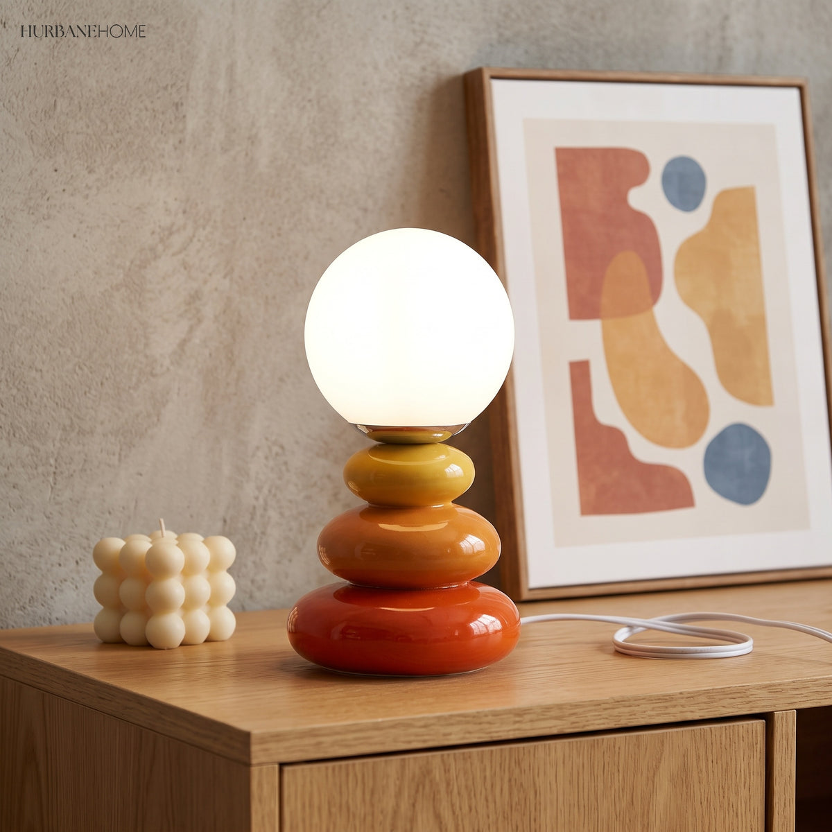 Orange stacked lamp lit beside a framed abstract print and candle