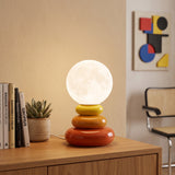 Orange stacked table lamp with a white glass globe on a wood sideboard