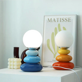 Blue and orange stacked lamps lit side by side on a pale plinth