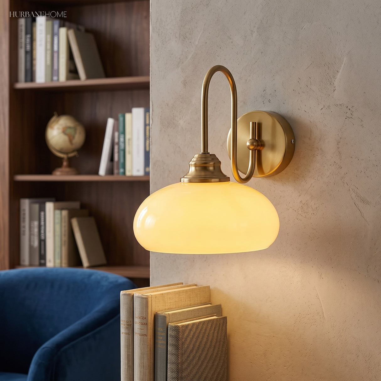 Milk glass wall sconce lit beside a bookshelf and blue armchair