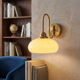 Milk glass wall sconce lit beside a bookshelf and blue armchair