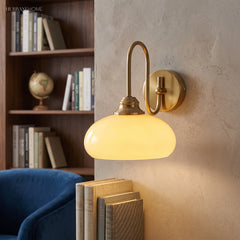 Milk glass wall sconce lit beside a bookshelf and blue armchair