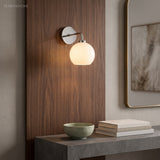 Milk glass sconce lit against a walnut panel above a stone console and books