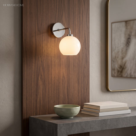 Milk glass sconce lit against a walnut panel above a stone console and books