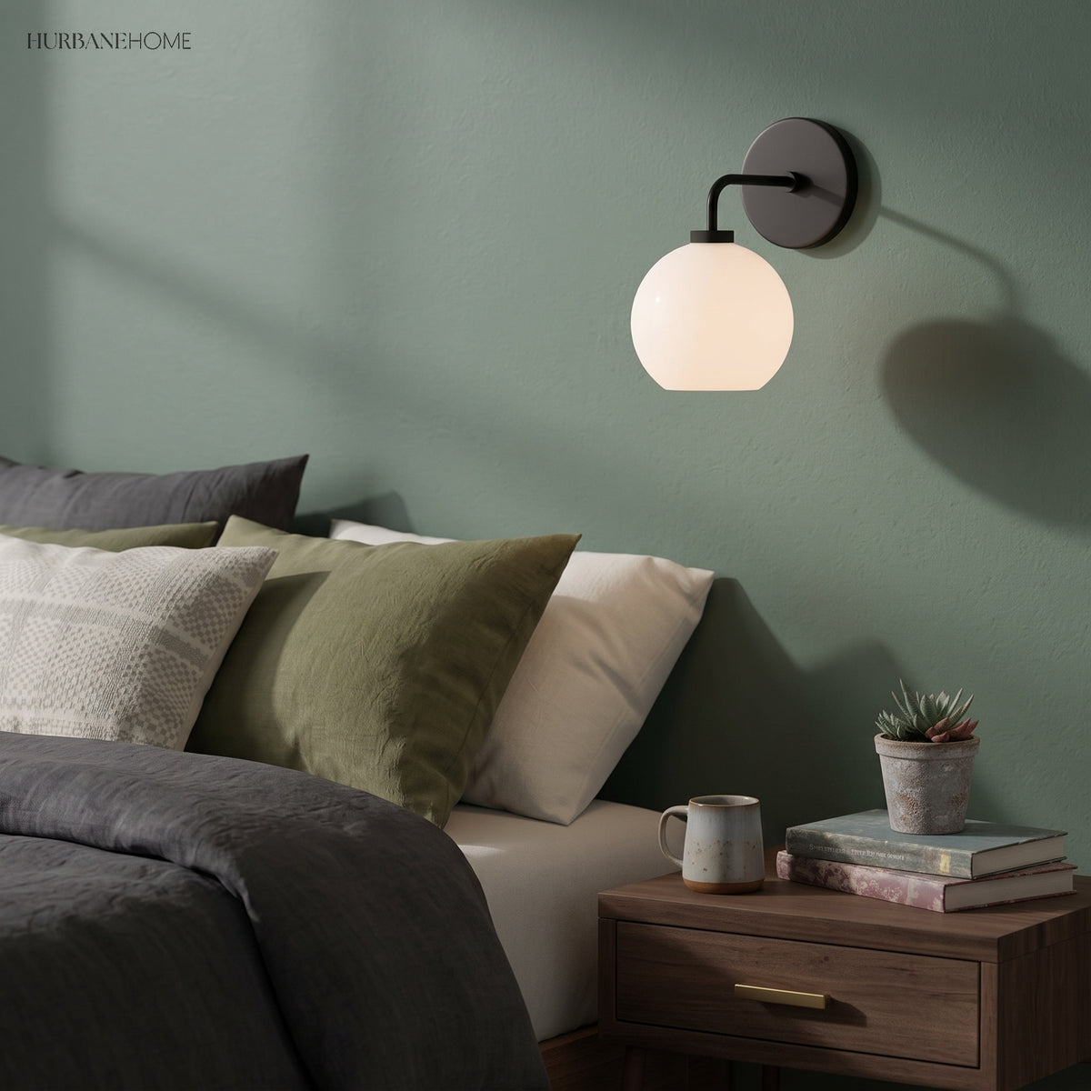Black globe sconce on a green bedroom wall above a timber bedside table
