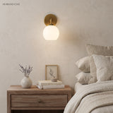 Brass globe sconce lit above an oak nightstand with dried lavender and books