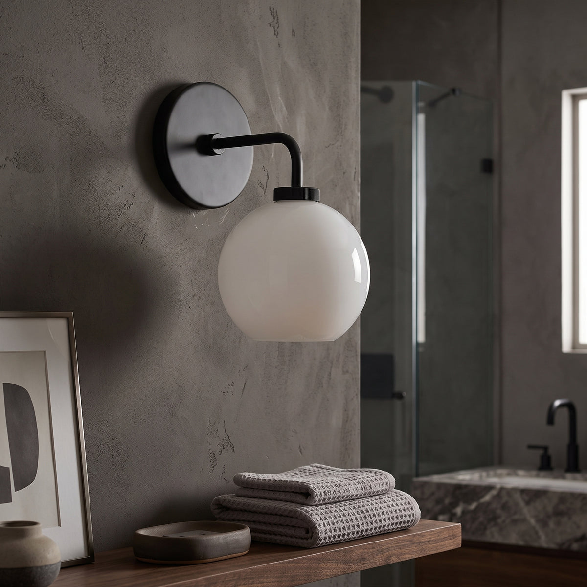 Black milk glass globe sconce on a concrete bathroom wall beside folded towels